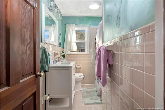 bathroom with a textured ceiling, tile walls, toilet, and vanity