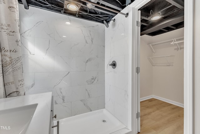 bathroom with a stall shower, a spacious closet, baseboards, and wood finished floors