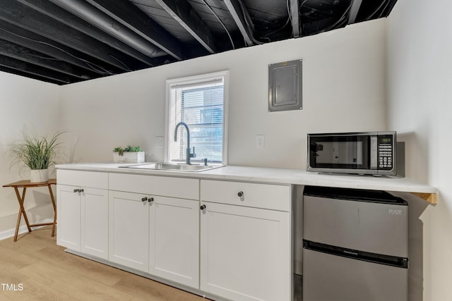 kitchen featuring light wood finished floors, light countertops, appliances with stainless steel finishes, white cabinetry, and a sink