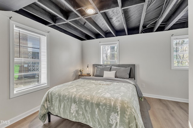 bedroom featuring multiple windows, beamed ceiling, baseboards, and wood finished floors