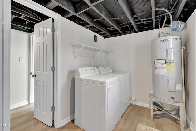 washroom featuring laundry area, baseboards, water heater, light wood-type flooring, and washing machine and clothes dryer