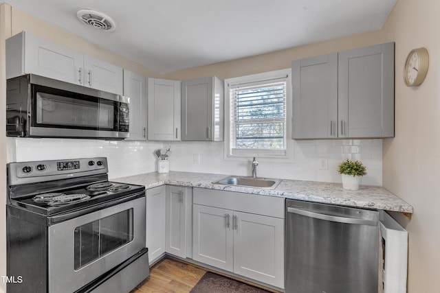 kitchen with light stone counters, stainless steel appliances, a sink, visible vents, and tasteful backsplash