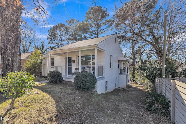 exterior space featuring covered porch, brick siding, and fence