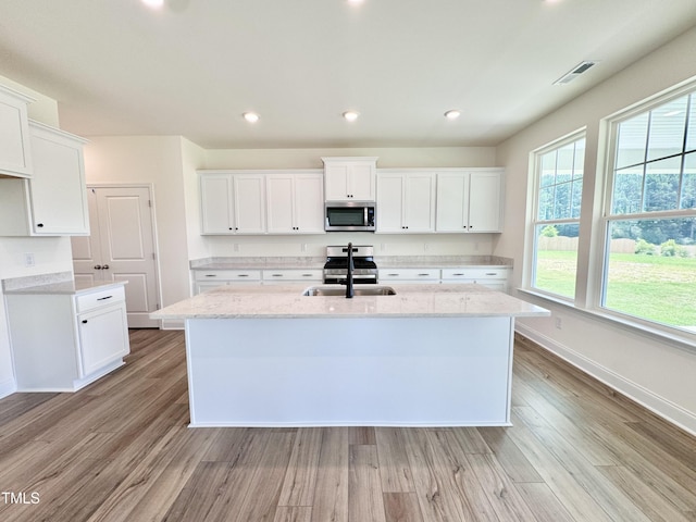 kitchen featuring a center island with sink, visible vents, appliances with stainless steel finishes, light wood-type flooring, and a sink