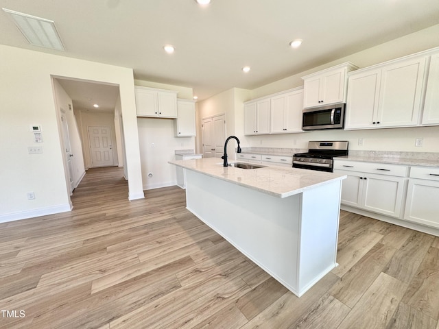 kitchen with light wood-style flooring, stainless steel appliances, a sink, white cabinetry, and a center island with sink