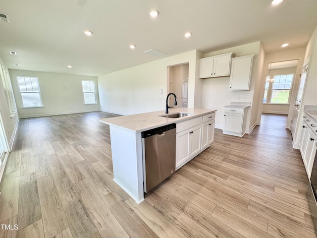 kitchen with light wood finished floors, light countertops, a kitchen island with sink, a sink, and dishwasher