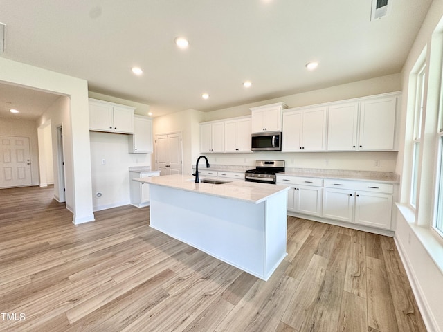 kitchen with stainless steel appliances, visible vents, light wood-style flooring, white cabinetry, and a sink