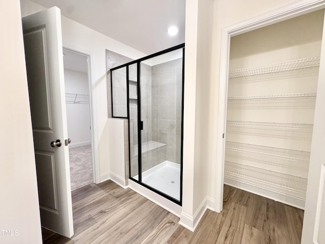 bathroom with wood finished floors, a shower stall, a walk in closet, and baseboards