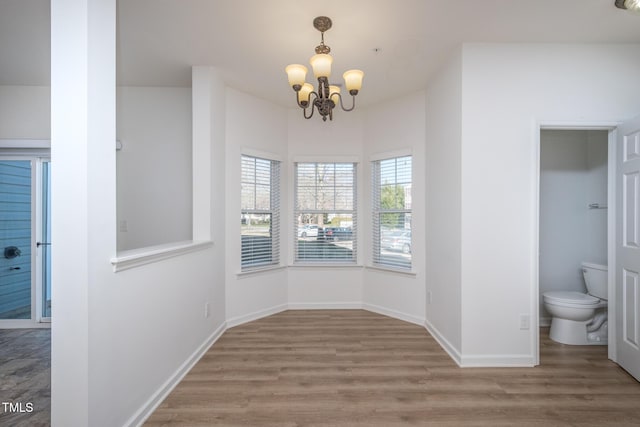 unfurnished dining area with a notable chandelier, wood finished floors, and baseboards