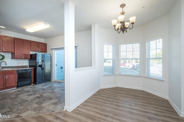 kitchen with baseboards, wood finished floors, hanging light fixtures, black appliances, and a sink