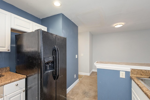 kitchen featuring black fridge with ice dispenser, white cabinets, and baseboards