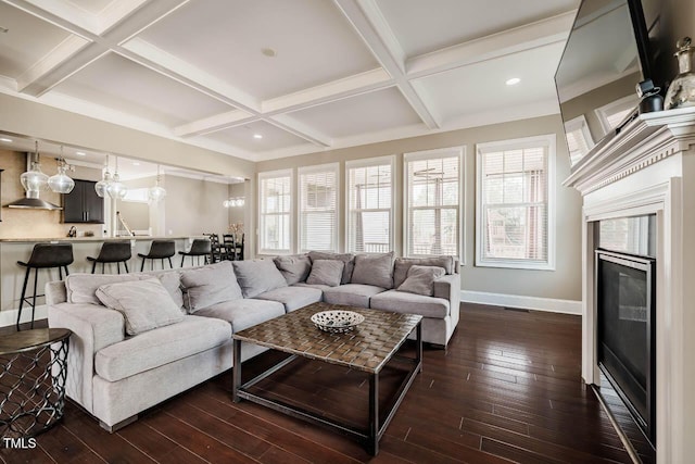 living room featuring beamed ceiling, dark wood-type flooring, a glass covered fireplace, and coffered ceiling