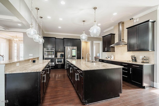 kitchen featuring a large island, wall chimney exhaust hood, appliances with stainless steel finishes, and a sink