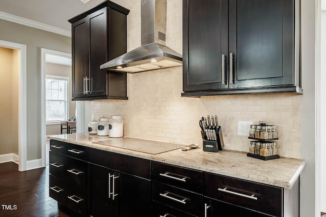 kitchen featuring light stone counters, tasteful backsplash, electric stovetop, wall chimney exhaust hood, and crown molding