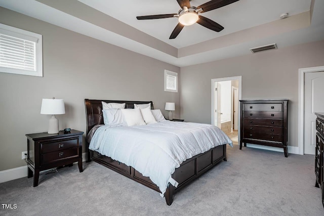 bedroom featuring a ceiling fan, visible vents, baseboards, a raised ceiling, and light colored carpet