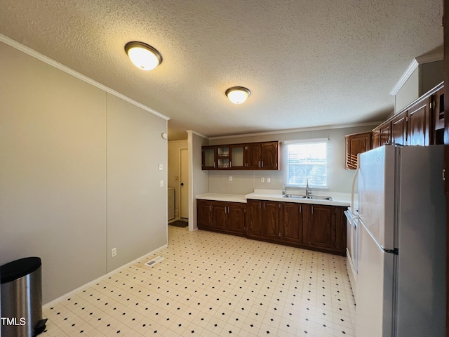 kitchen featuring crown molding, light countertops, freestanding refrigerator, a sink, and dark brown cabinets