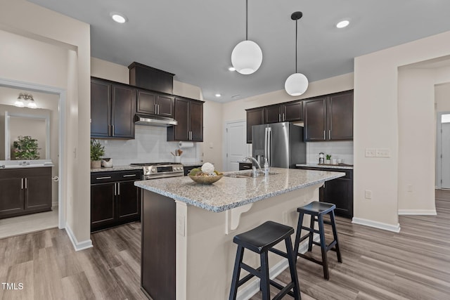 kitchen featuring stainless steel appliances, dark brown cabinetry, a sink, under cabinet range hood, and a kitchen breakfast bar