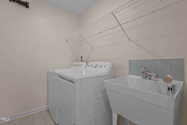 laundry room with light tile patterned flooring, laundry area, a sink, baseboards, and independent washer and dryer