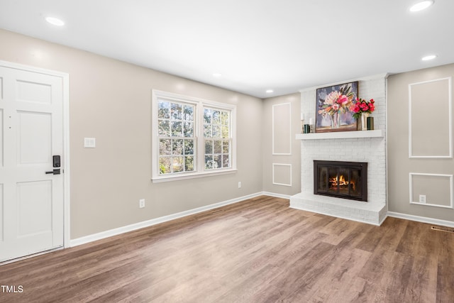 unfurnished living room featuring visible vents, baseboards, a brick fireplace, and wood finished floors