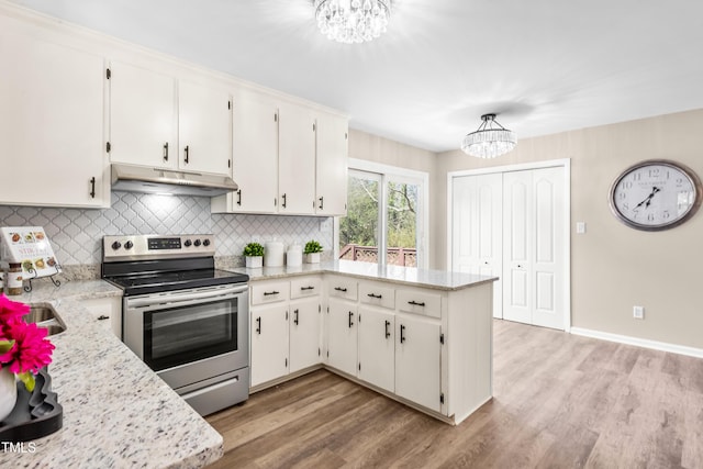 kitchen with a peninsula, light wood-style flooring, stainless steel electric stove, under cabinet range hood, and a notable chandelier