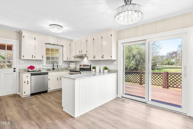 kitchen with under cabinet range hood, appliances with stainless steel finishes, a peninsula, a notable chandelier, and a sink