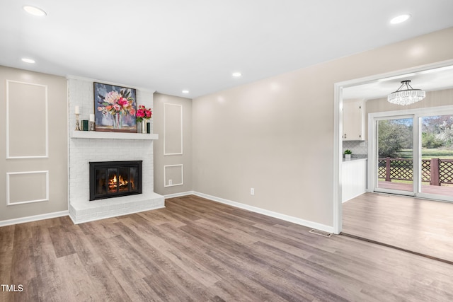 unfurnished living room with a brick fireplace, recessed lighting, wood finished floors, and baseboards