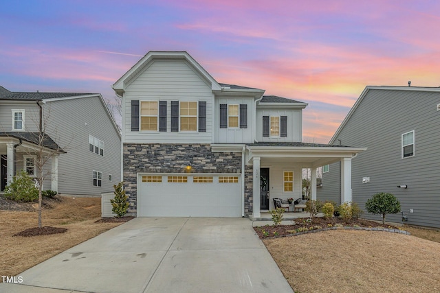 view of front of home with covered porch, a garage, driveway, stone siding, and board and batten siding