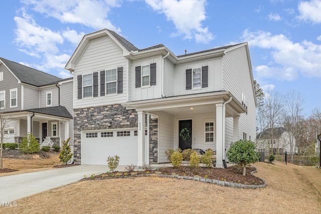 view of front of property featuring stone siding, fence, an attached garage, board and batten siding, and driveway