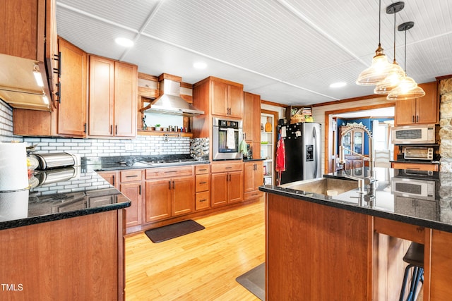 kitchen with light wood-type flooring, decorative light fixtures, tasteful backsplash, stainless steel appliances, and wall chimney exhaust hood