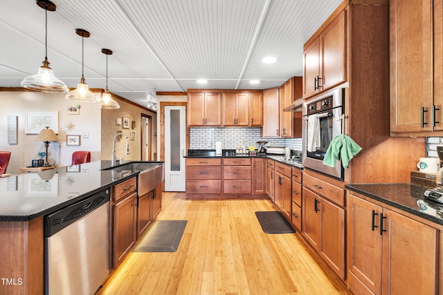 kitchen with a sink, stainless steel appliances, brown cabinets, and light wood-type flooring