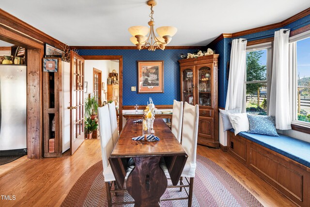 dining space featuring light wood-type flooring, ornamental molding, an inviting chandelier, wallpapered walls, and baseboards