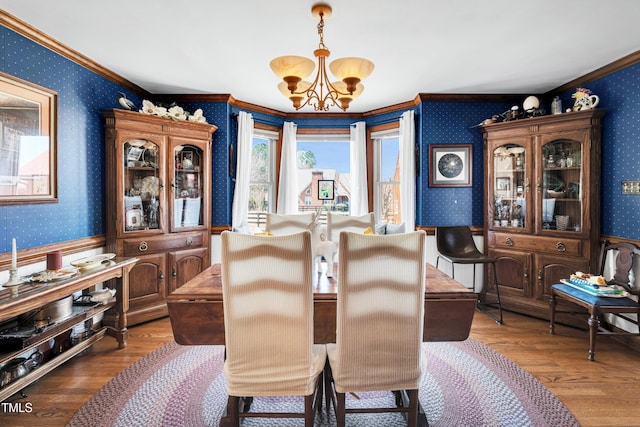 dining space with wood finished floors, a chandelier, crown molding, and wallpapered walls