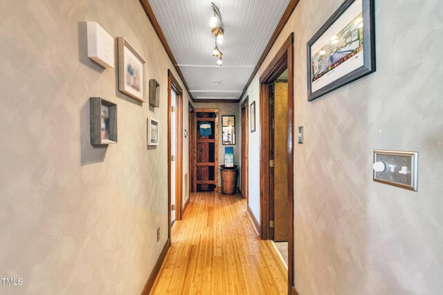 corridor featuring track lighting, baseboards, and light wood finished floors