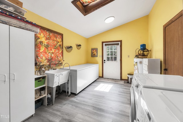 clothes washing area with washer and dryer, water heater, a skylight, light wood finished floors, and laundry area