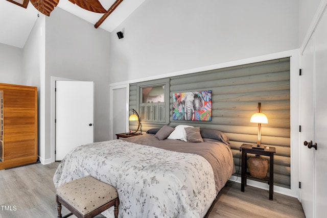 bedroom with a closet, light wood-style flooring, high vaulted ceiling, and log walls