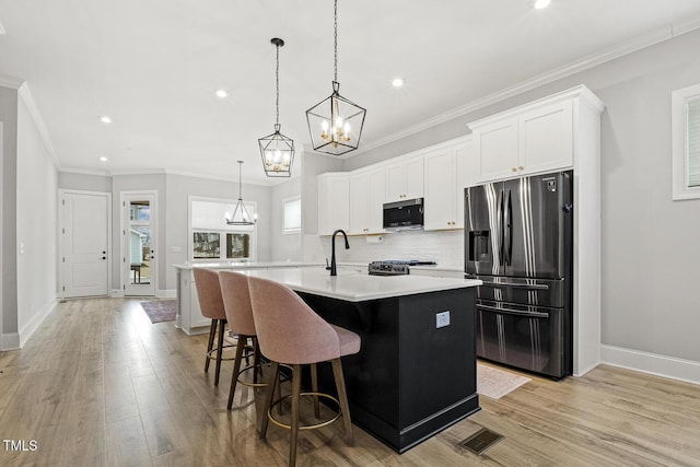 kitchen with stainless steel appliances, light countertops, decorative backsplash, a sink, and an island with sink