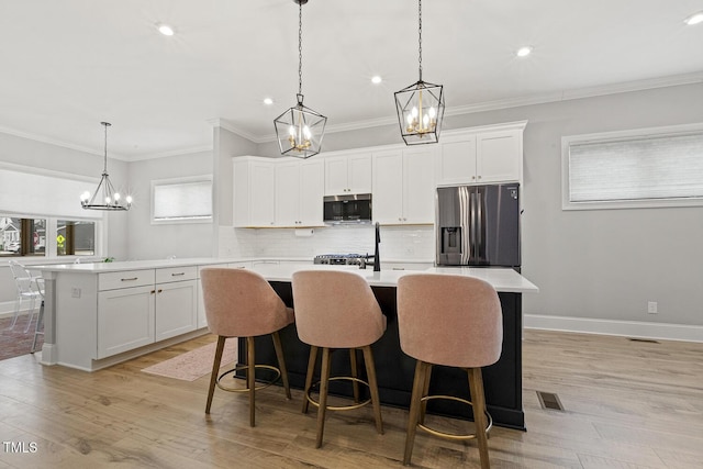 kitchen with an island with sink, light wood finished floors, appliances with stainless steel finishes, and light countertops