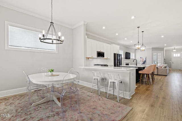 kitchen with crown molding, light countertops, light wood-style floors, fridge with ice dispenser, and a kitchen bar