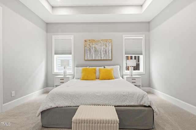 carpeted bedroom featuring baseboards and a tray ceiling