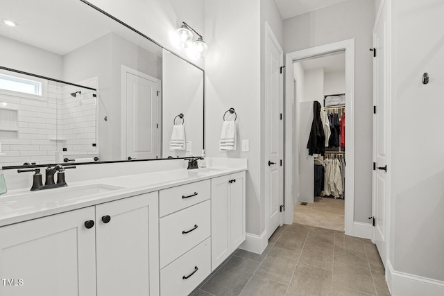 full bath featuring double vanity, a spacious closet, a tile shower, and a sink