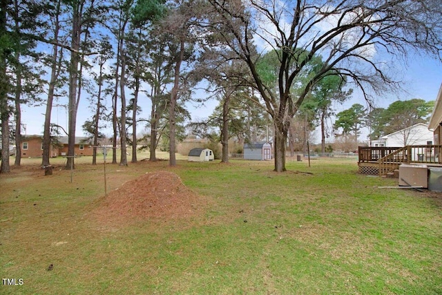 view of yard featuring a storage shed, an outdoor structure, a wooden deck, and fence