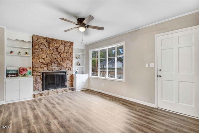 unfurnished living room with a stone fireplace, wood finished floors, built in shelves, and baseboards