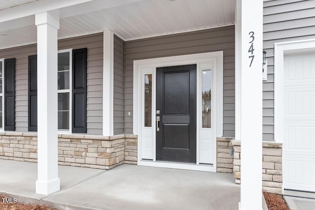 doorway to property featuring an attached garage, stone siding, and a porch