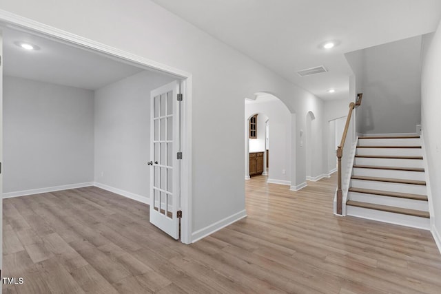 corridor with arched walkways, recessed lighting, visible vents, light wood-type flooring, and baseboards