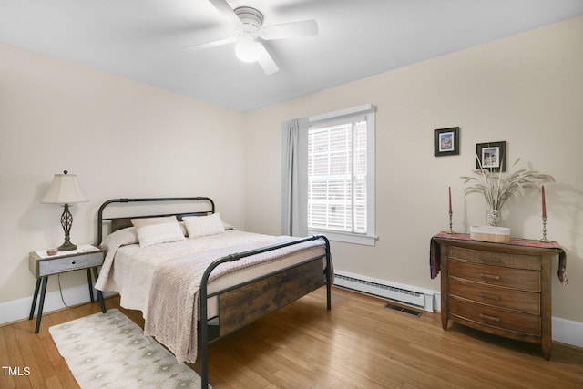 bedroom with a baseboard heating unit, light wood-type flooring, visible vents, and baseboards