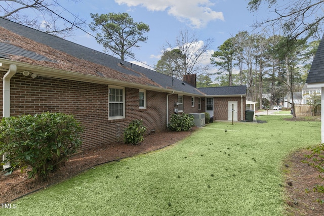 rear view of property with a yard, brick siding, a chimney, and central AC unit