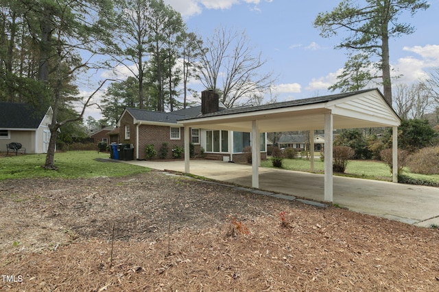 exterior space featuring an outbuilding, an attached carport, brick siding, a front lawn, and a chimney