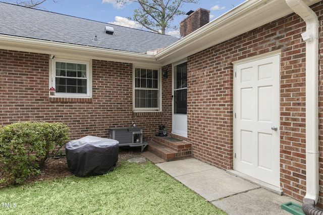 view of exterior entry with roof with shingles and brick siding