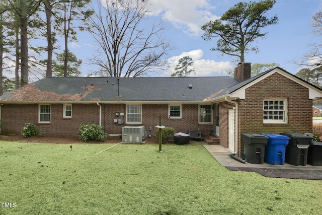 rear view of property with central air condition unit, brick siding, a shingled roof, a yard, and a chimney