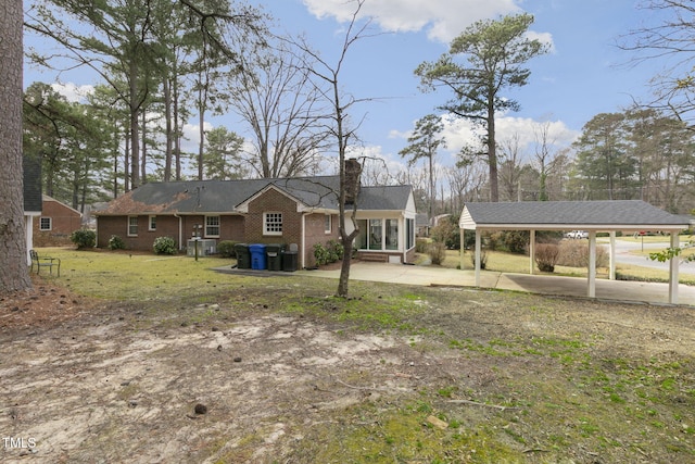 view of front of house featuring brick siding, a chimney, a detached carport, a front yard, and driveway